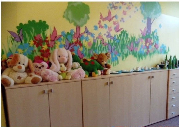 Szafki stojące pod ścianą pomalowaną w obrazki. Na szafkach zabawki pluszowe.