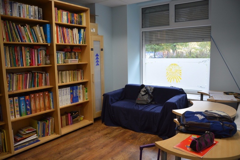 Zdjęcie Pomieszczenia z oknem, kanapą, stolikami i dużym regałem z książkami.