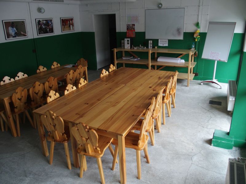 Zdjęcie przestrzeni z drewnianymi stołami i krzesłami. Na ścianie tablica. 