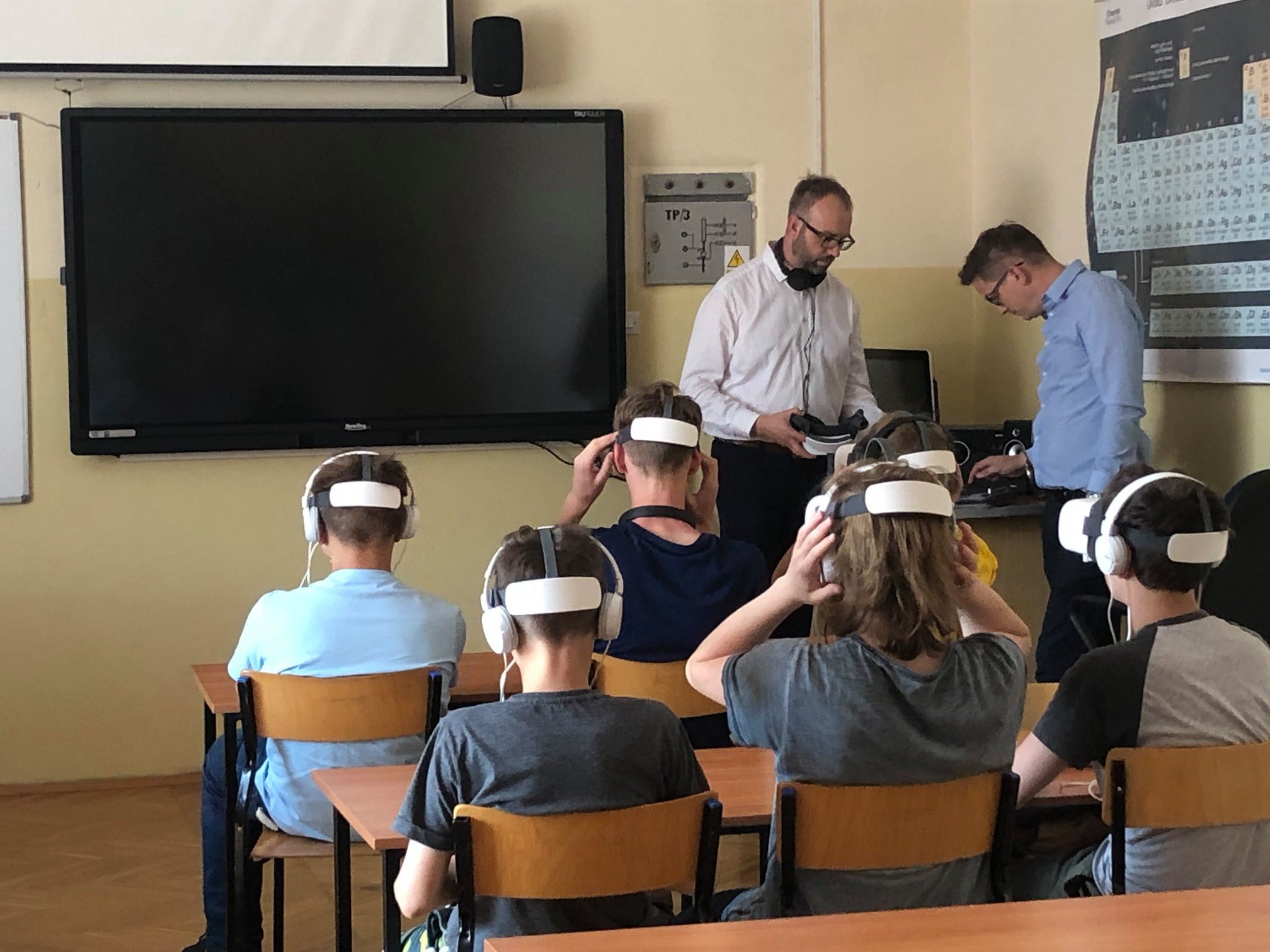 Kilka uczniów siedzi na krzesłach, każda z tych osób ma założone okulary VR - z wirtualną rzeczywistością.