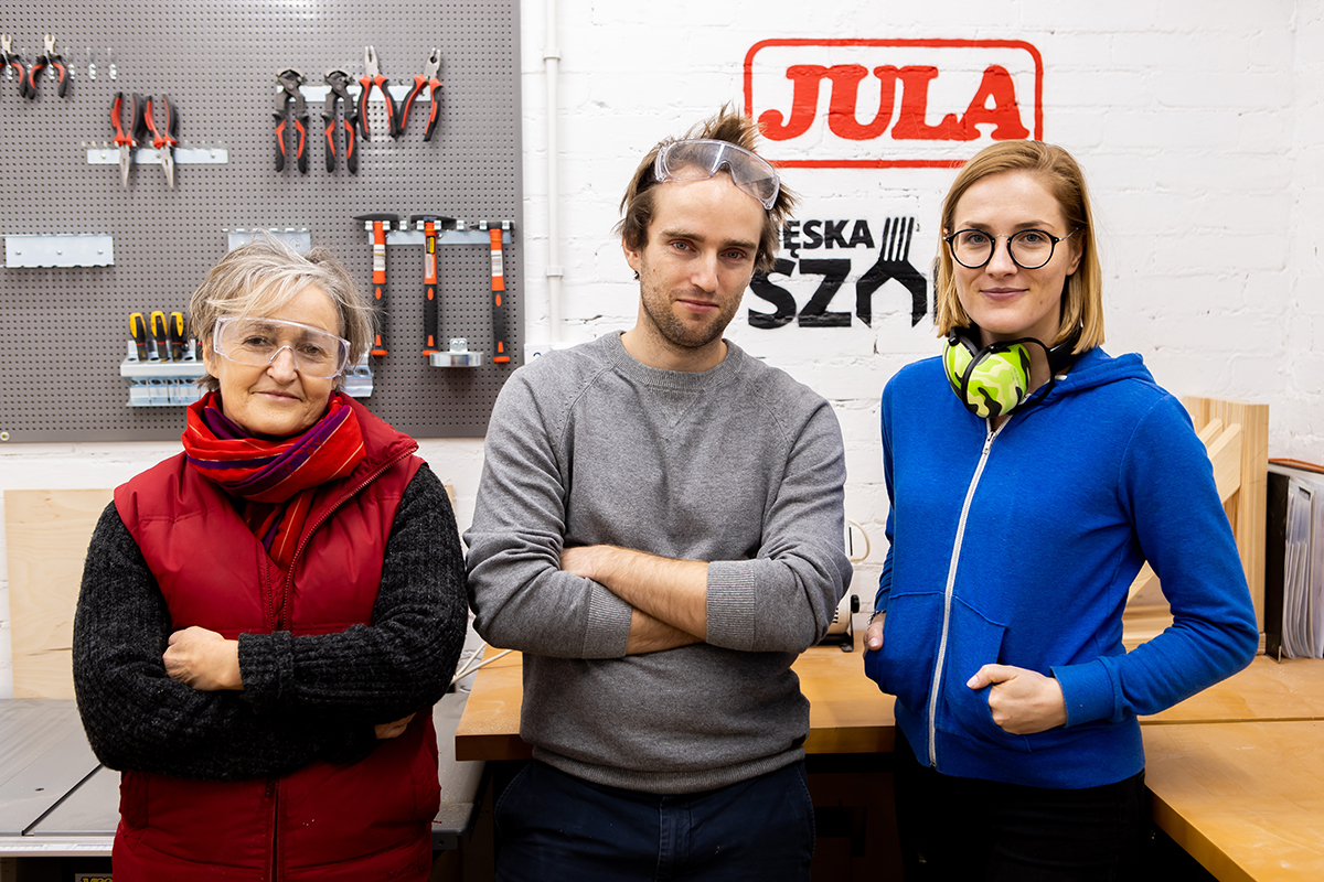 Trzy osoby, mężczyzna w środku i dwie kobiety po bokach ustawione na tle napisu: Jula. Męska Szopa.