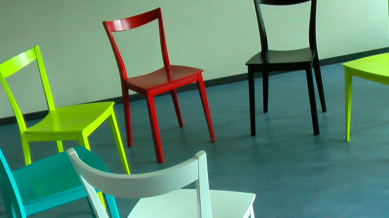 Sześć krzeseł w rożnych kolorach ustawionych na podłodze w kręgu.