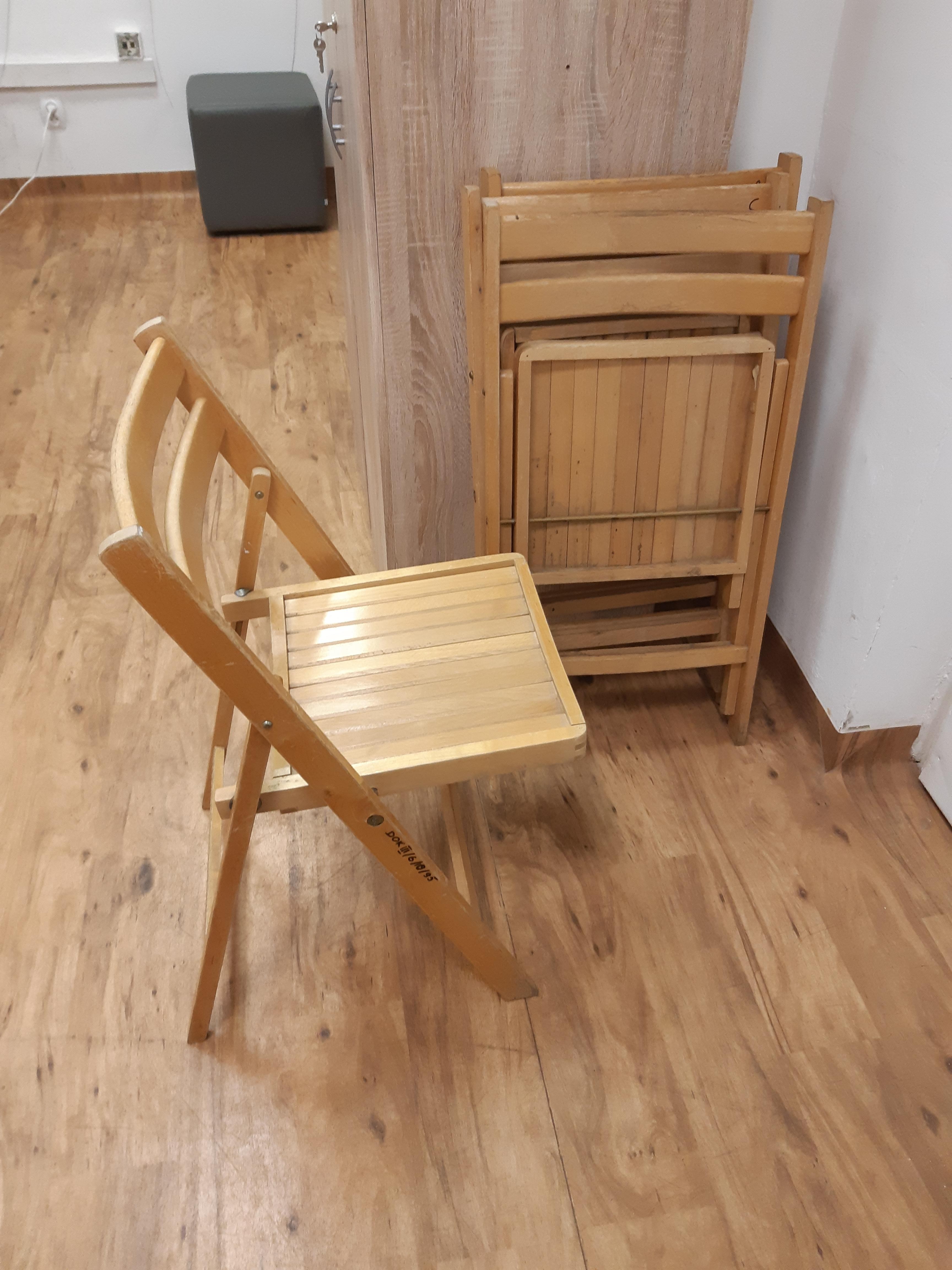 Rozłożone drewniane krzesło i dwa złożone, oparte o ścianę.